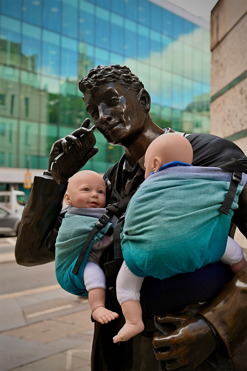 Statue of a LIFFE (London International Financial Futures and Options Exchange) trader on the phone with two model babies in blue slings across his chest